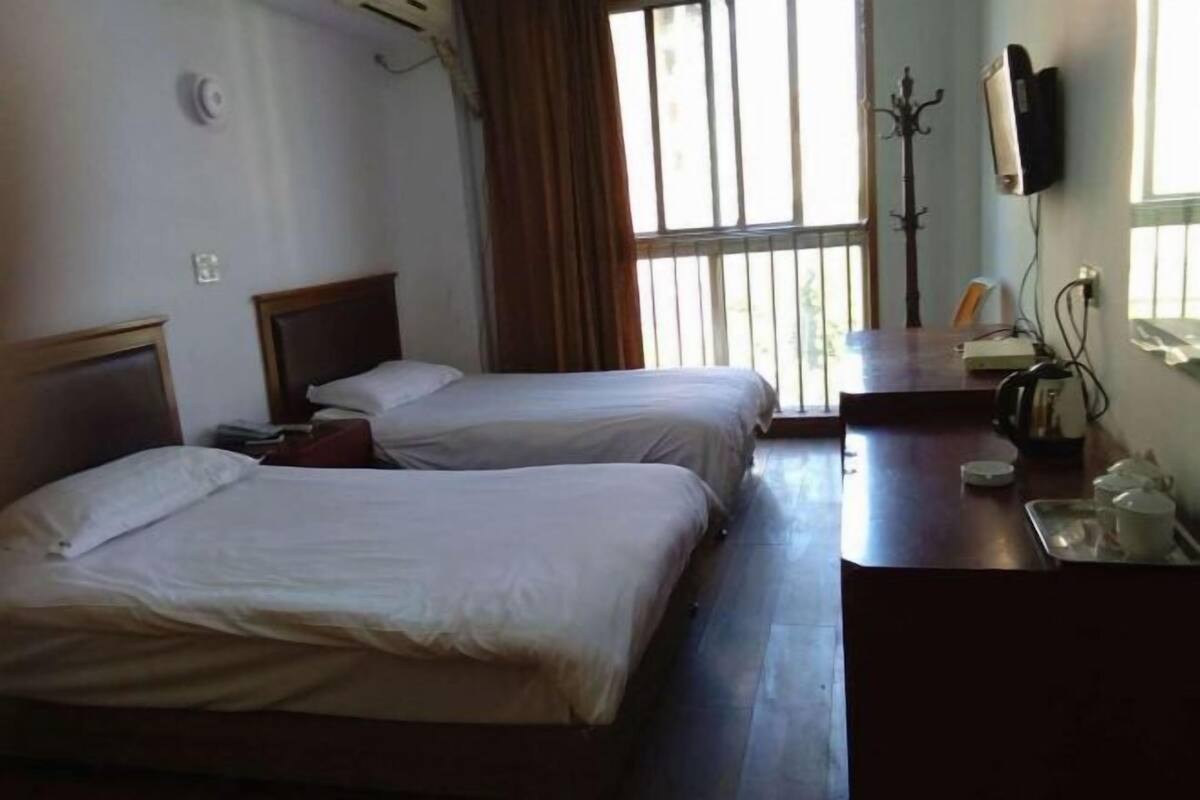 Habitación de hotel con dos camas, un escritorio con silla, televisor montado en la pared y ventana con cortinas.