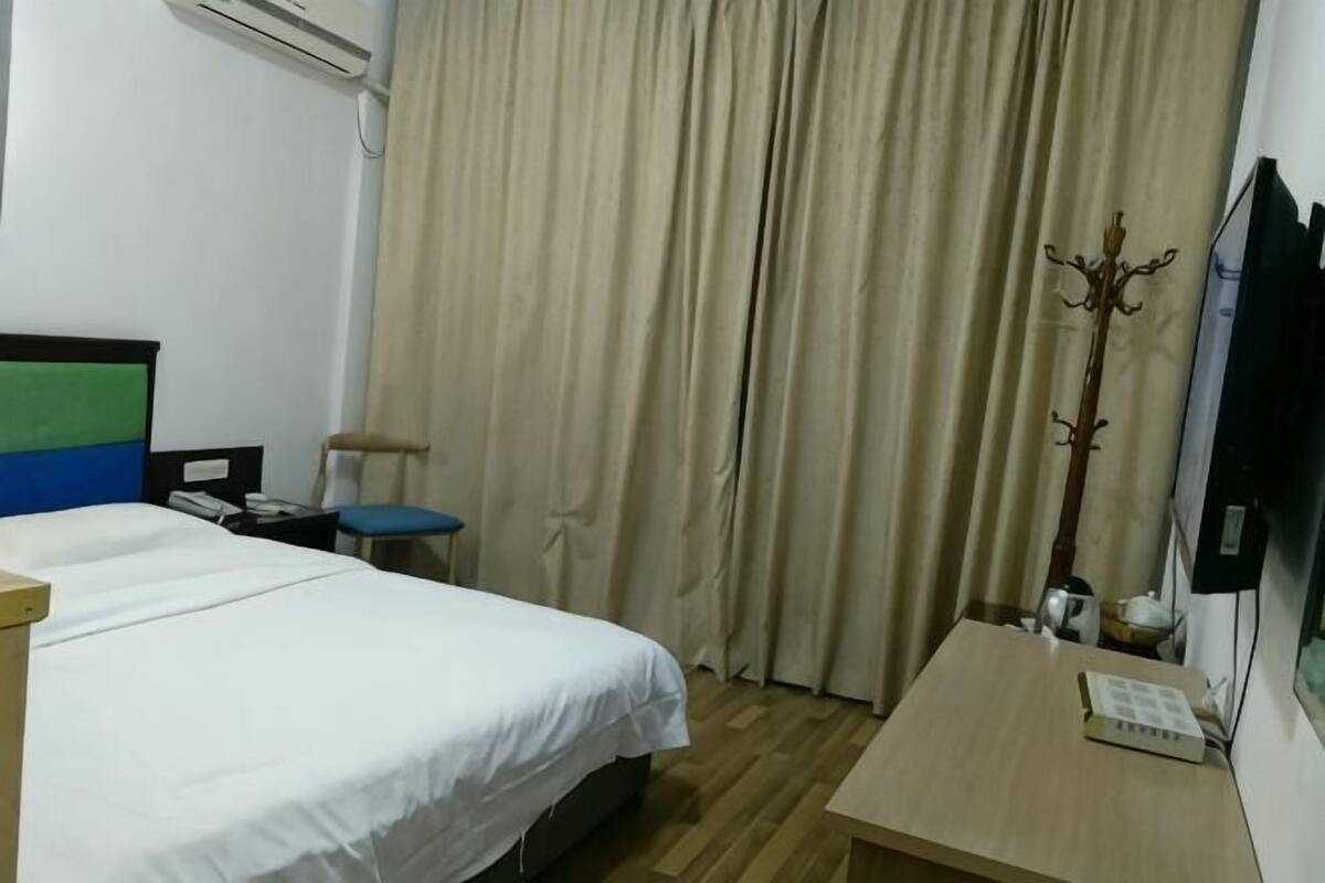 Una habitación de hotel con cama, escritorio, silla, perchero y televisión.