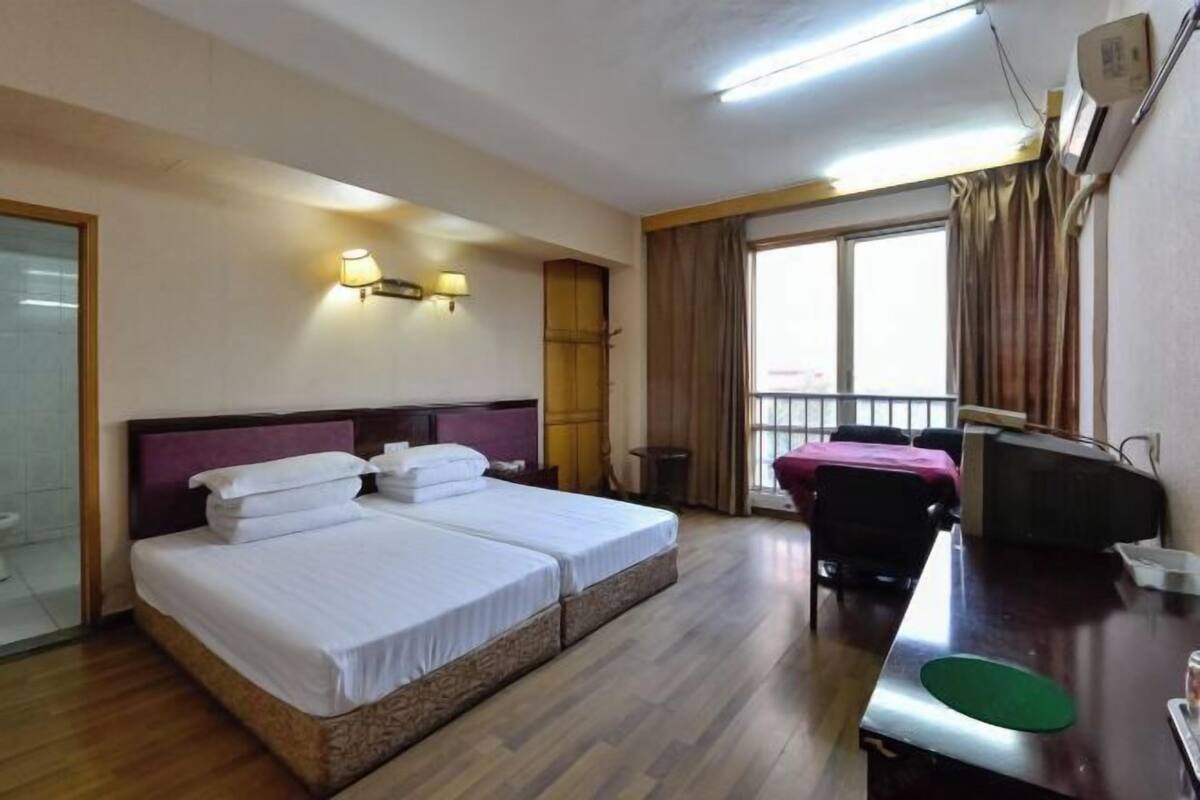 Habitación de hotel con dos camas, un escritorio, una silla, un ventanal con cortinas y un balcón.
