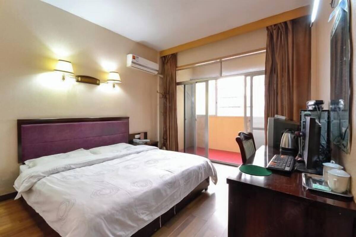 Habitación de hotel con cama, escritorio con computadora, cafetera y puerta corrediza al balcón.