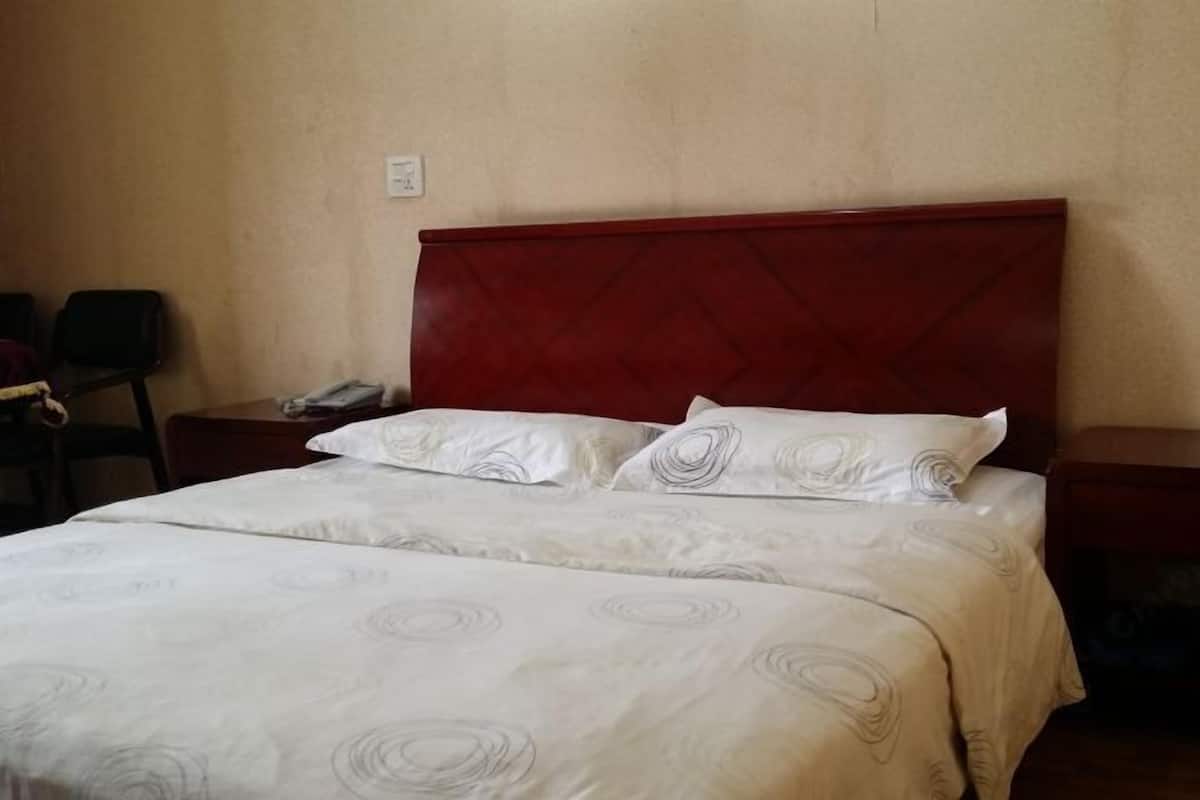 Una habitación de hotel con una cama, cabecera de madera, mesita de noche y una silla.