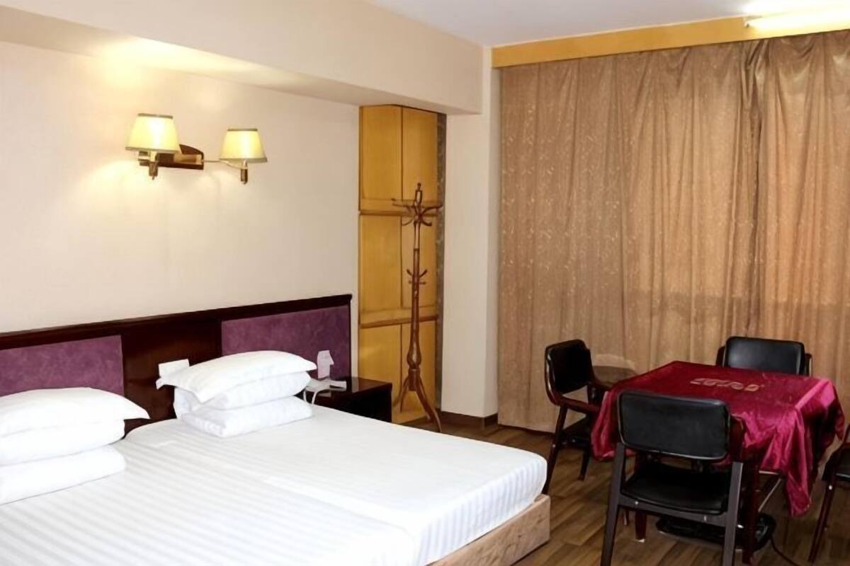 Una habitación de hotel con cama, lámparas de noche, un escritorio con silla y un ventanal con cortinas.