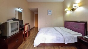 A hotel room with a bed, a television on a wooden cabinet, a desk with a chair, and wall-mounted lamps. - Xingyuan Hotel (Taizhou)