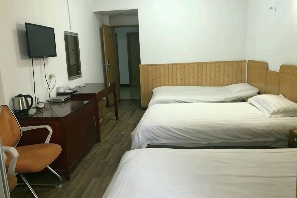 Habitación de hotel con tres camas, un escritorio con silla, televisión y puerta que da a otra habitación.