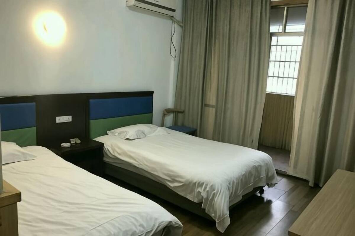 Habitación de hotel con dos camas, una mesita de noche, aire acondicionado instalado en la pared y una ventana con cortinas.