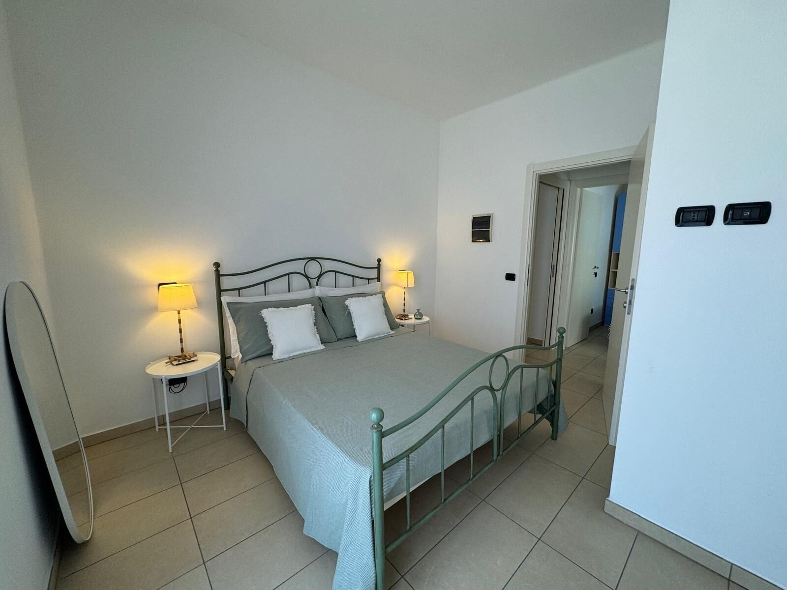 Una camera da letto con un letto, due comodini, una lampada, uno specchio e una porta.