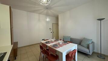 Zona pranzo con tavolo bianco, sedie rosse e due lampade a sospensione.