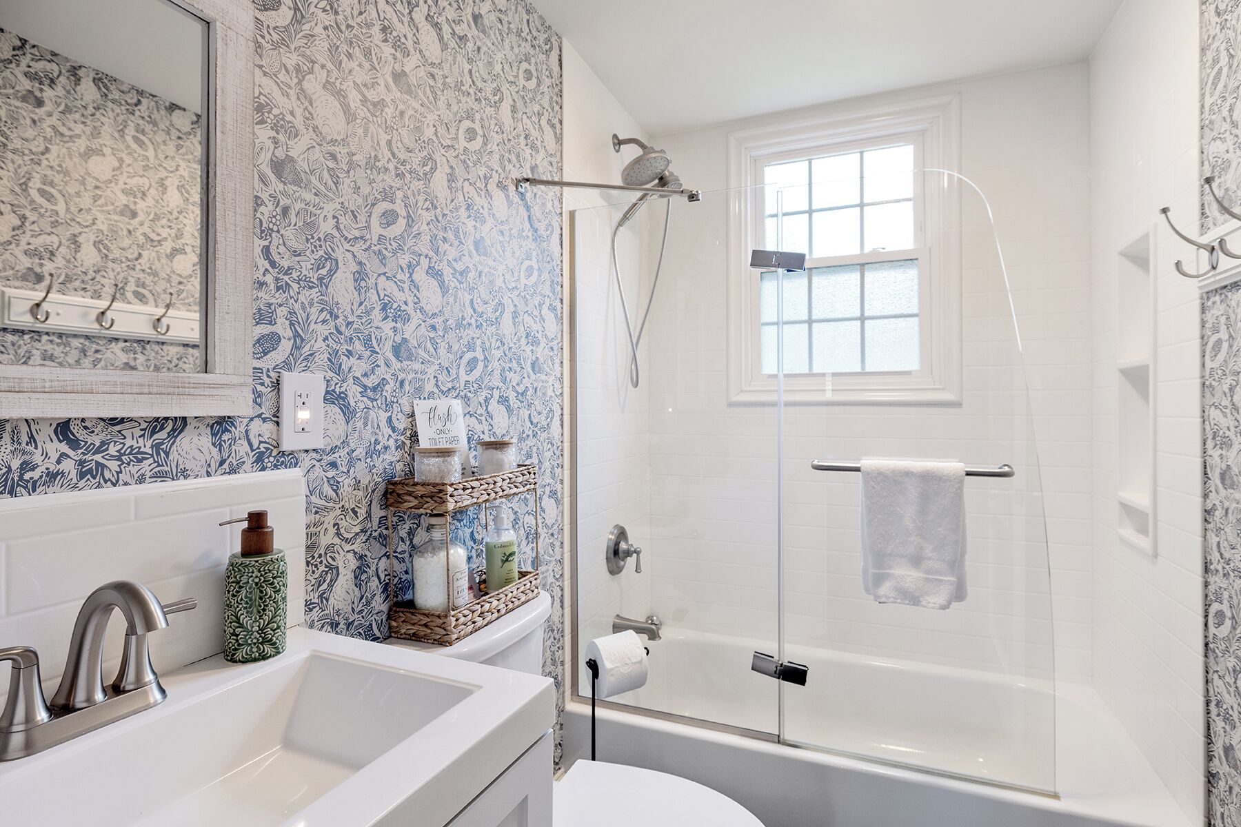 Une salle de bain avec une douche, des toilettes et un lavabo. Il y a une fenêtre au-dessus de la douche, et on peut voir un porte-serviettes.
