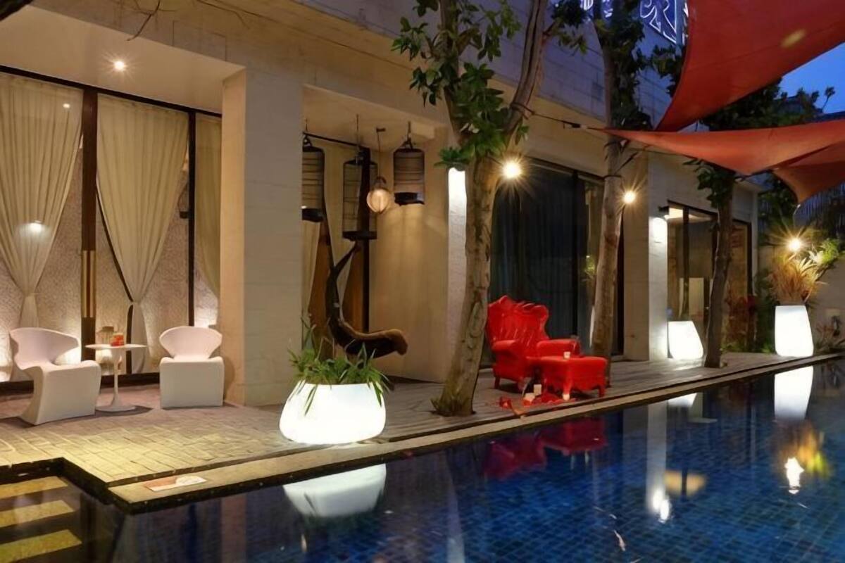 A poolside area with lounge chairs, a red chair, and a well-lit indoor space.
