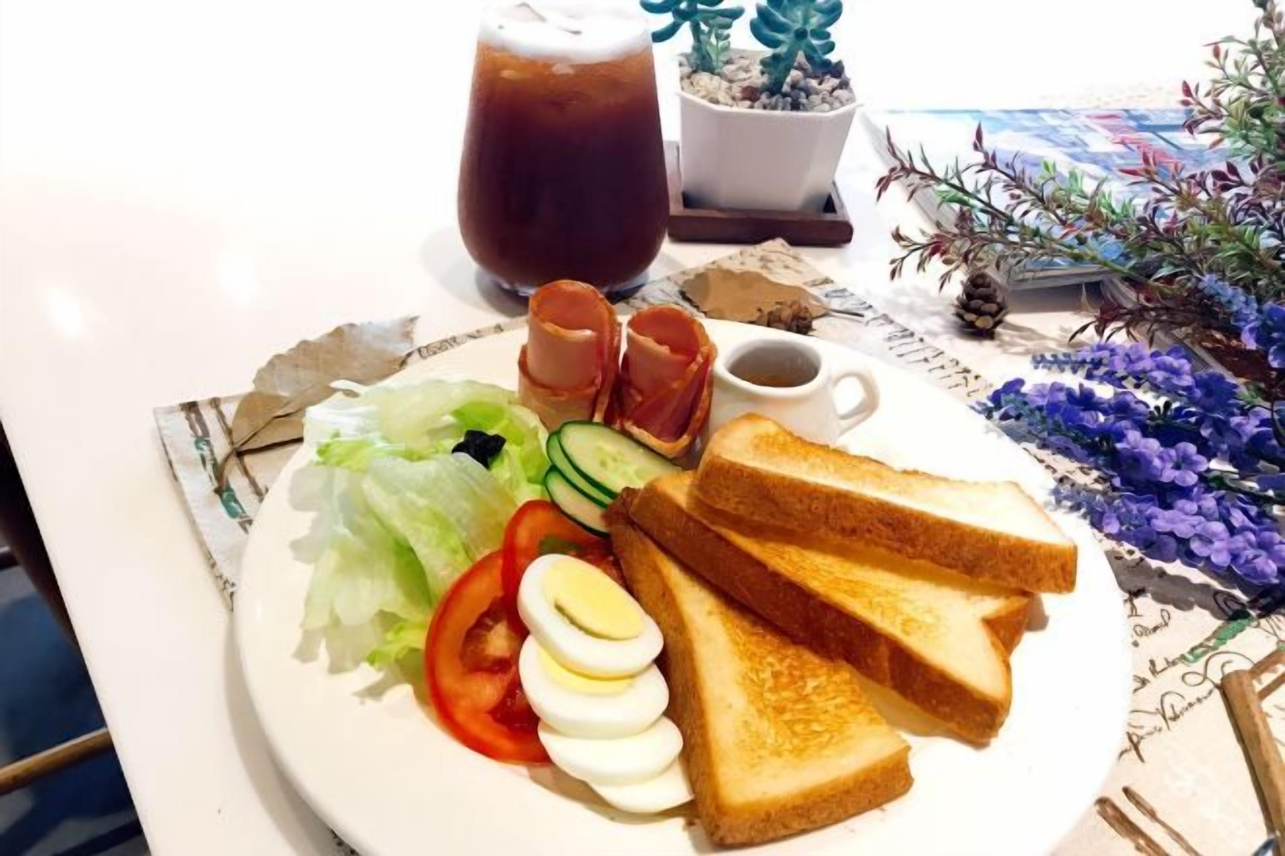 A plate with toast, eggs, vegetables, and a drink on a table with a notebook and decorative plants.