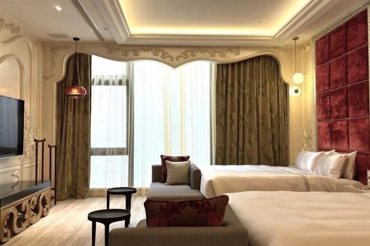 A hotel room with a large bed, a smaller sofa, a TV, and a seating area with a table.