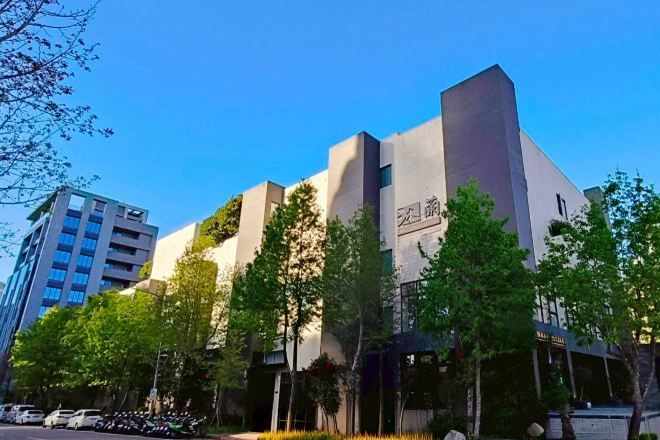 A modern building with a prominent entrance, surrounded by trees and parked cars.