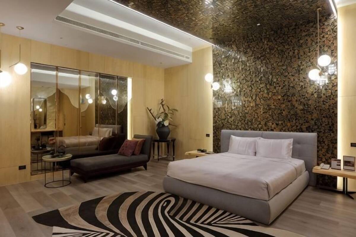 A modern bedroom with a large bed, a sofa, a mirror, and a decorative wall.