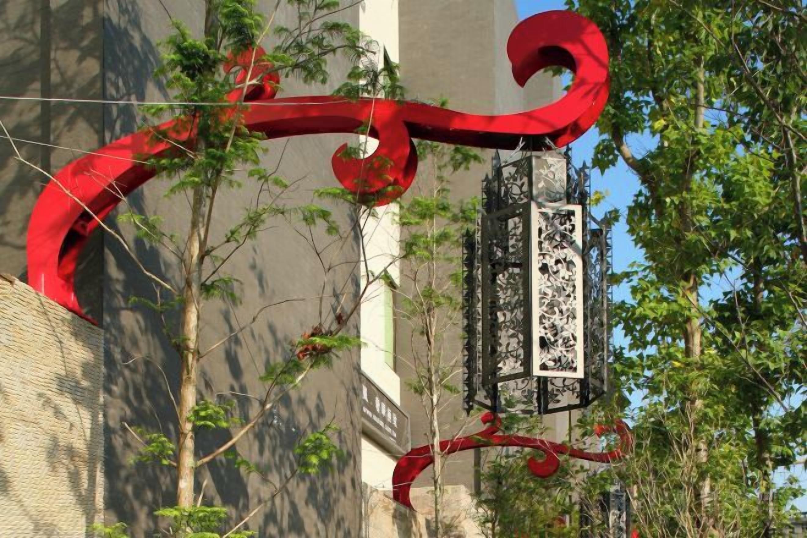 A red metal structure with a rectangular sign, surrounded by trees and a building.