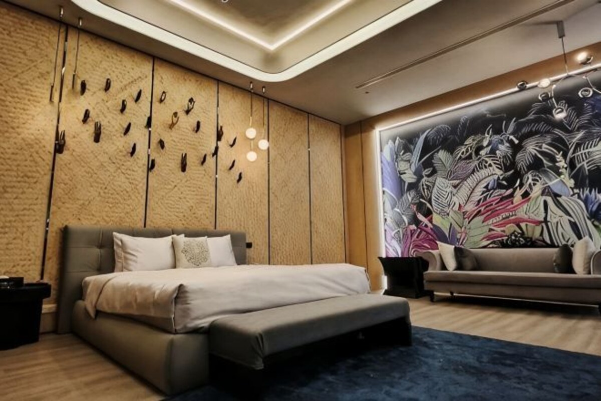 A modern bedroom with a bed, a sofa, a wall mural, and a unique light fixture.