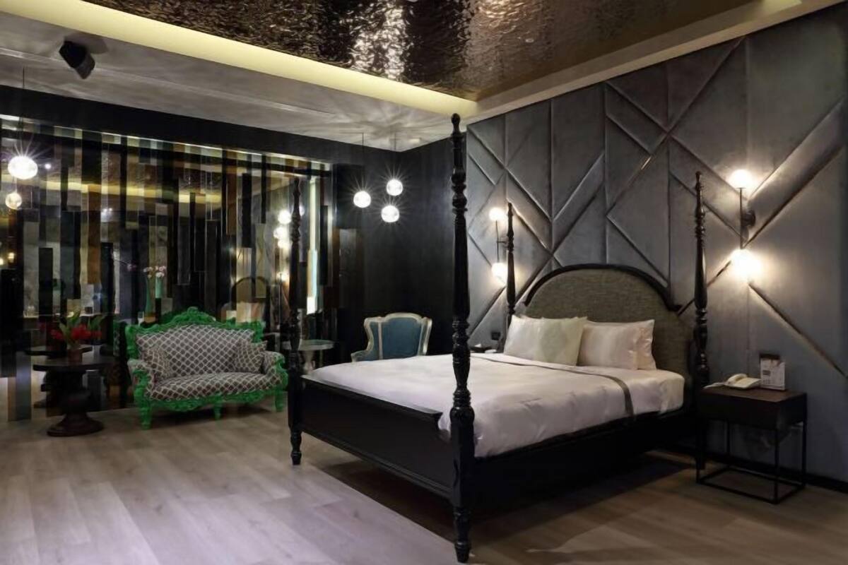 A bedroom with a four-poster bed, a green sofa, a chair, and a small table.