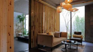A modern living room with a sofa, a coffee table, and a chair. There is a large window providing a view of greenery outside.