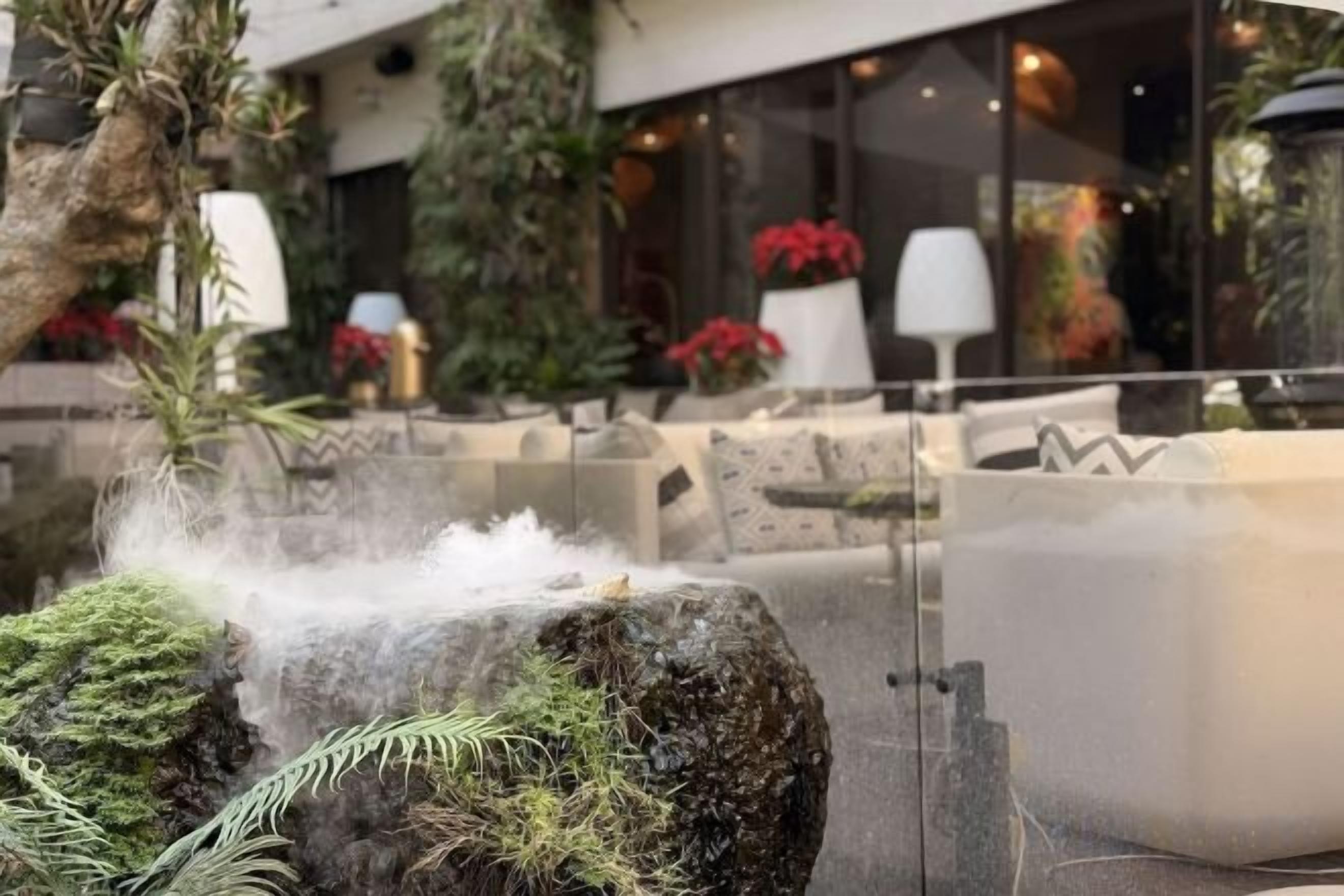 A water feature with a rock, mist, and indoor seating area with chairs and tables.