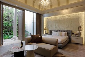 A modern bedroom with a large bed, a sofa, a coffee table, and a view of greenery outside.
