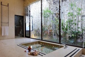 Un cuarto de spa con un ventanal grande, una bañera y un pequeño jardín interior.