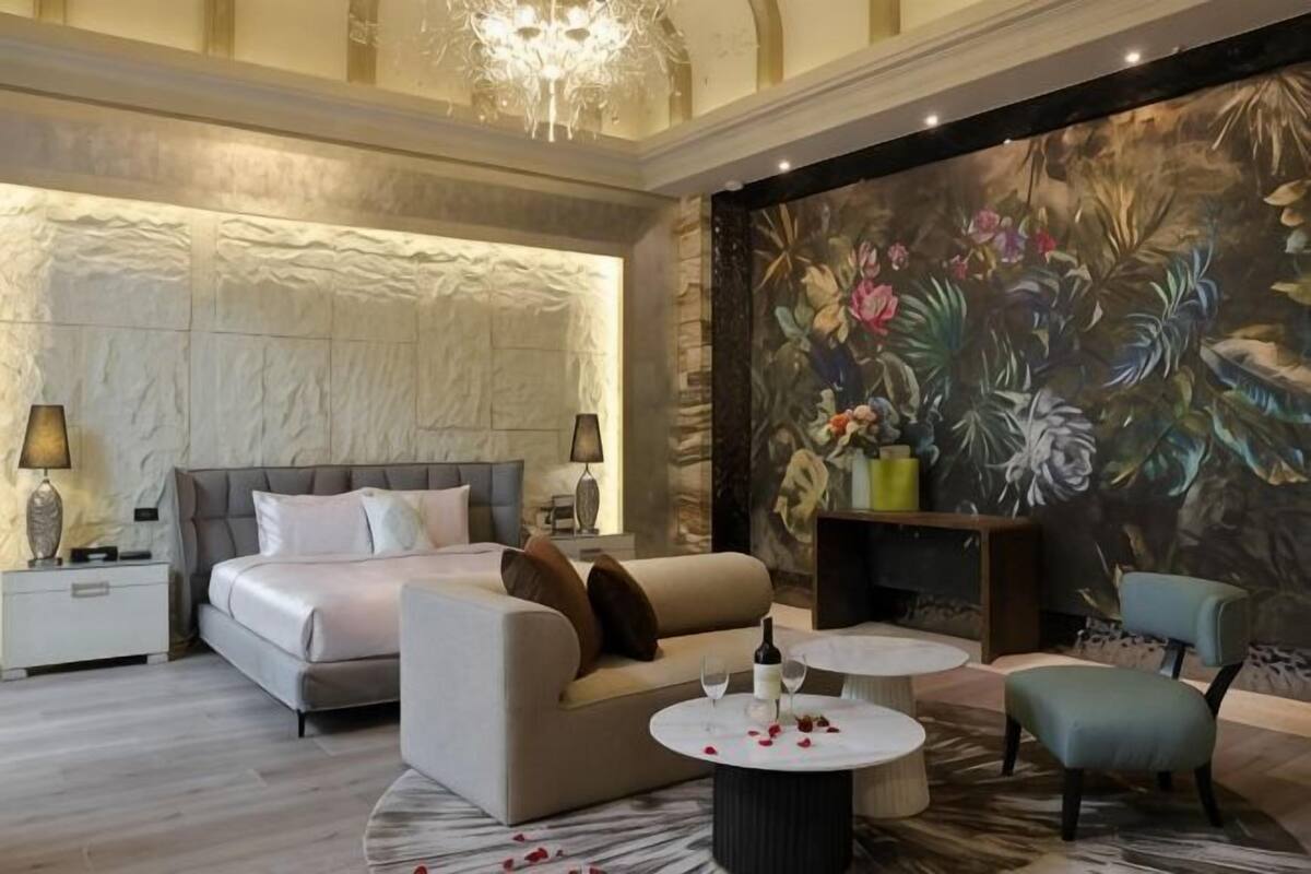 A bedroom with a large bed, a sofa, a coffee table, and a mural.