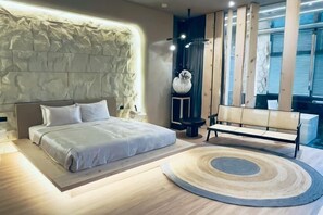 A bedroom with a large bed, a round rug, a bench, and a decorative wall.