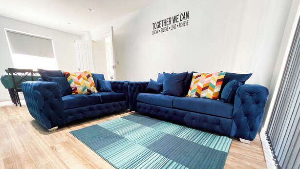 Een moderne woonkamer met een hoekbank, een kamerbreed tapijt en een inspirerende muisquote.