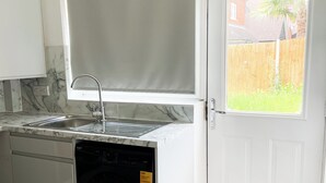 Een compacte keuken met een inbouw wasmachine, een spoelbak en een raam met uitzicht op een achtertuin.