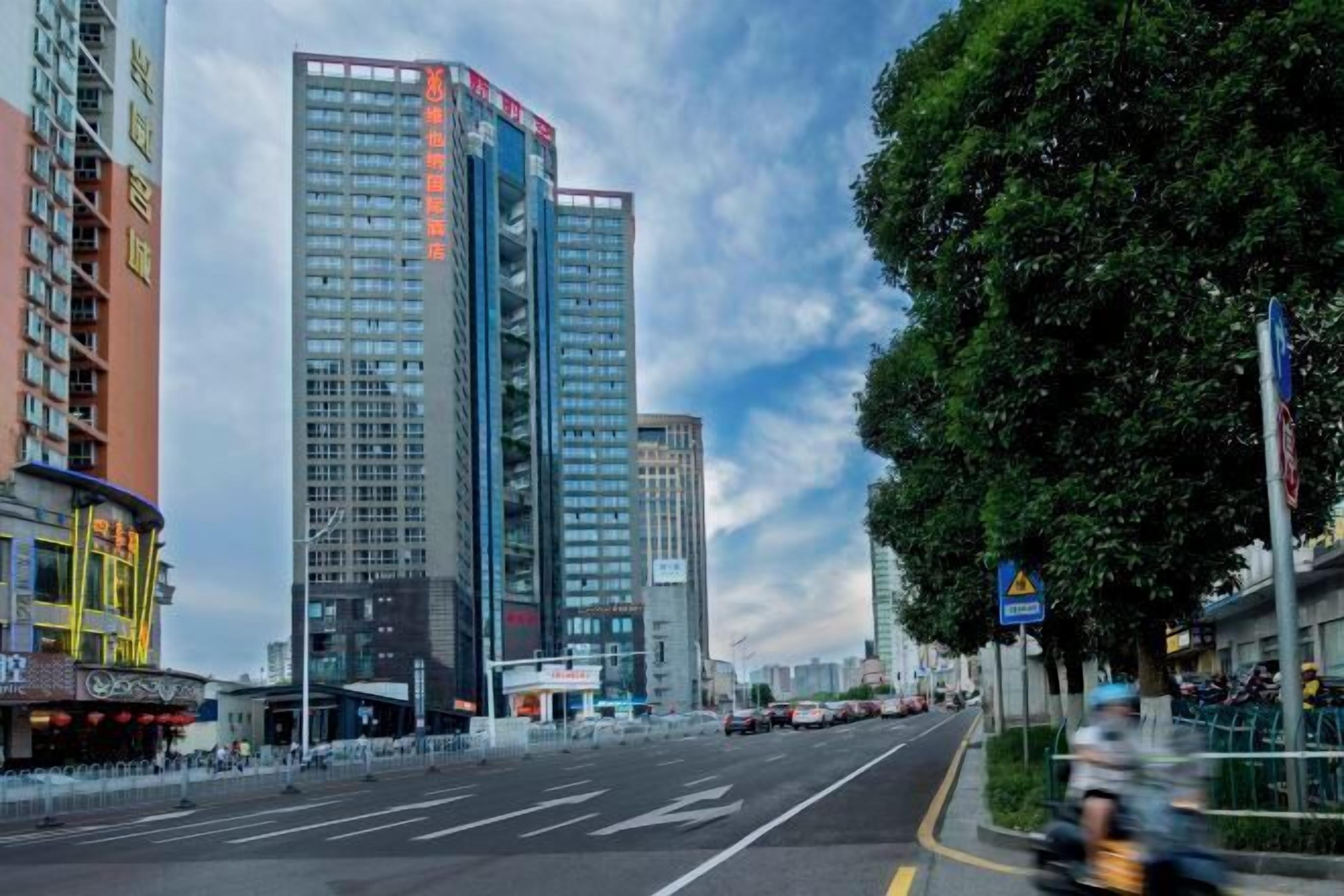 A modern high-rise building with multiple floors, large windows, and a prominent red sign on the top.