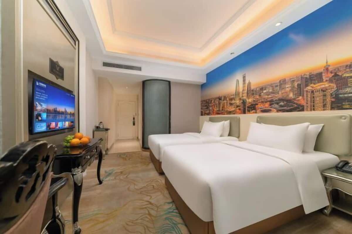 A hotel room with two beds, a television on the left, and a cityscape mural on the wall.