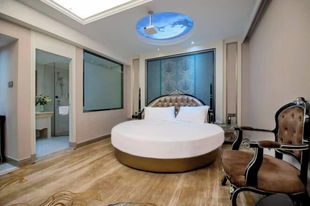 A modern bedroom with a round bed, a glass shower enclosure, and a skylight.