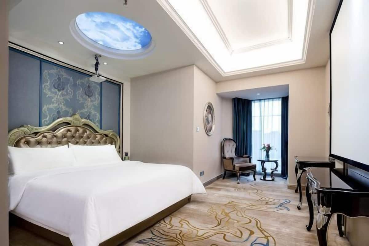 A hotel room with a large bed, a ceiling skylight, a desk, and a chair.