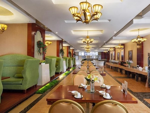 A hotel dining area with multiple tables and chairs, a long counter, and a row of green sofas. - Vienna International Hotel (Changsha)