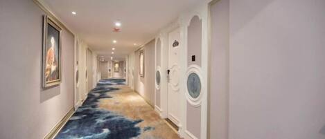 A hotel corridor with a patterned carpet, white walls, and doors with circular windows.