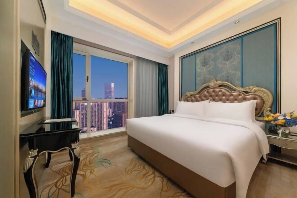 A hotel room with a large bed, a TV, a desk, and a view of a cityscape.