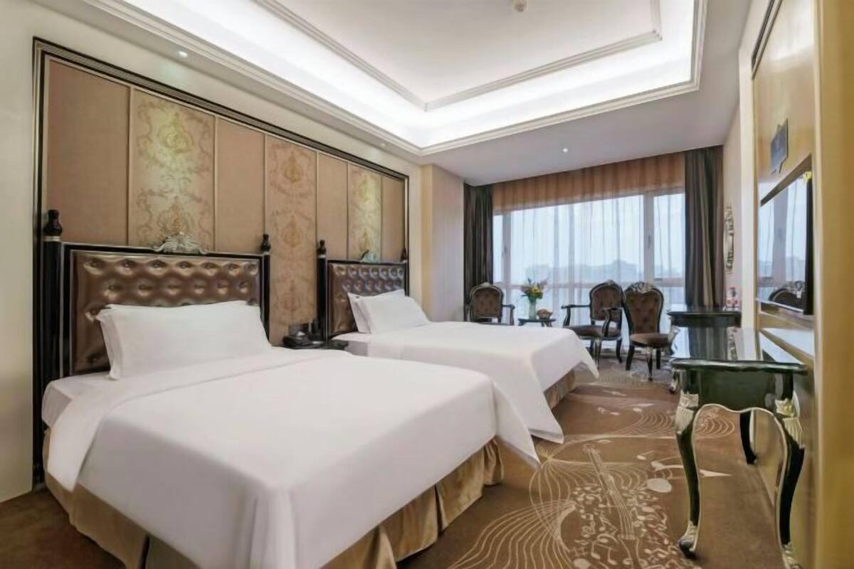 A hotel room with two beds, a large window with a view, and a seating area with chairs and a table.