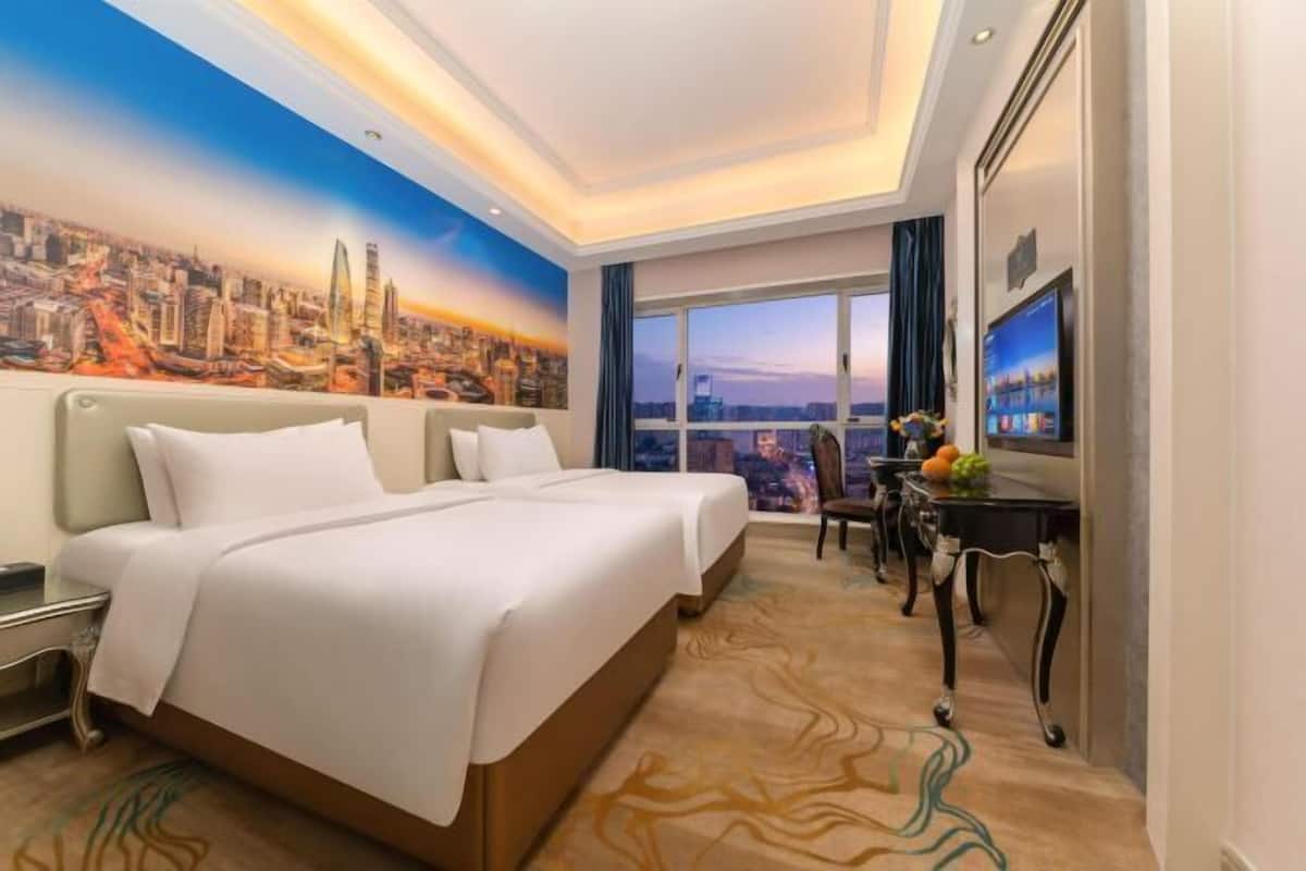 A hotel room with a large bed, a desk, and a cityscape mural on the wall.