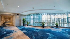 A spacious lobby with a blue carpet, a curved ceiling, and a large window with a view. - Vienna International Hotel (Changsha)