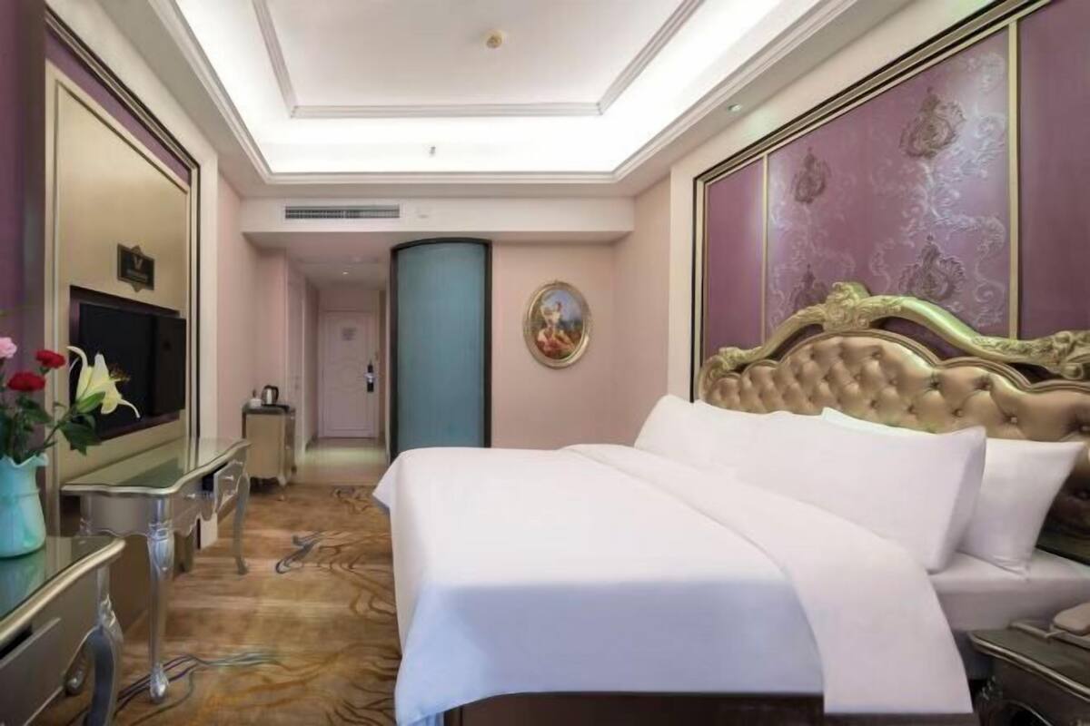 A hotel room with a large bed, a television, a desk, and a mirror.