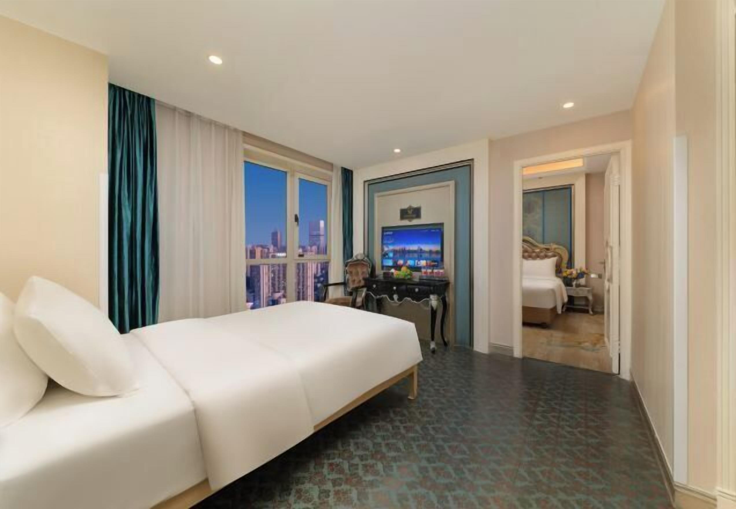 Hotelkamer met een groot bed, een bureau met een computer en uitzicht op een stadsbeeld.