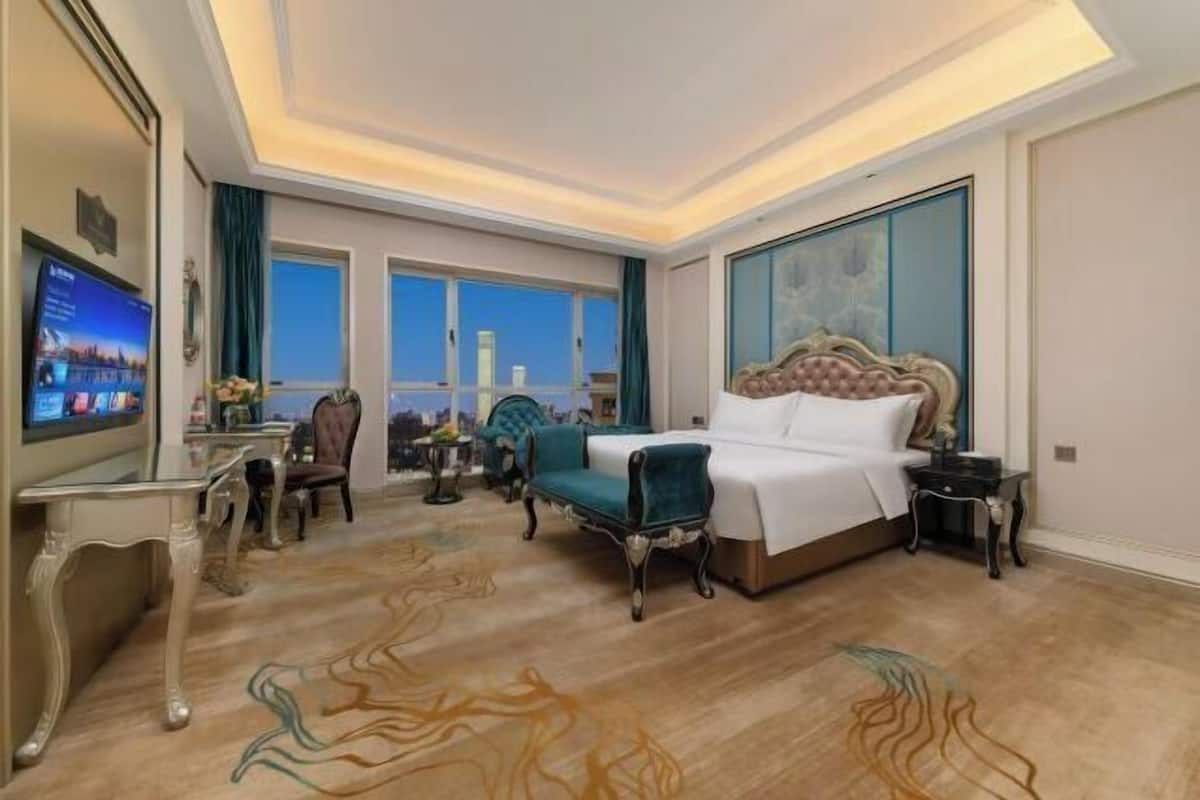 A hotel room with a large bed, a TV, a desk, and a view of the city.
