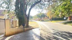 Un trottoir pavé, situé à côté d’une route, bordé d’arbres et délimité par une clôture en métal.