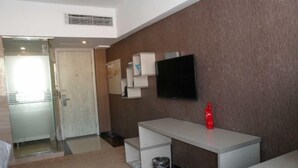 Una habitación de hotel con cama, escritorio, televisor, bote de basura y puerta.