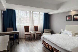Habitación de hotel con cama, escritorio, dos sillas, una mesita y ventana con cortinas.