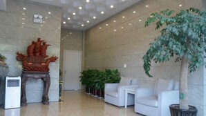 Un hall con piso de mármol, sofás blancos, un gran árbol en maceta y un adorno en la pared.