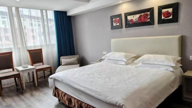 Habitación de hotel con una cama grande, una mesita pequeña, dos sillas y una ventana con cortinas.