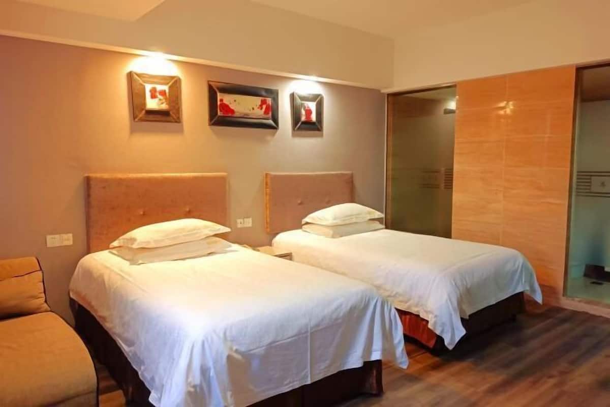 A hotel room with two beds, a sofa, and a glass shower enclosure.