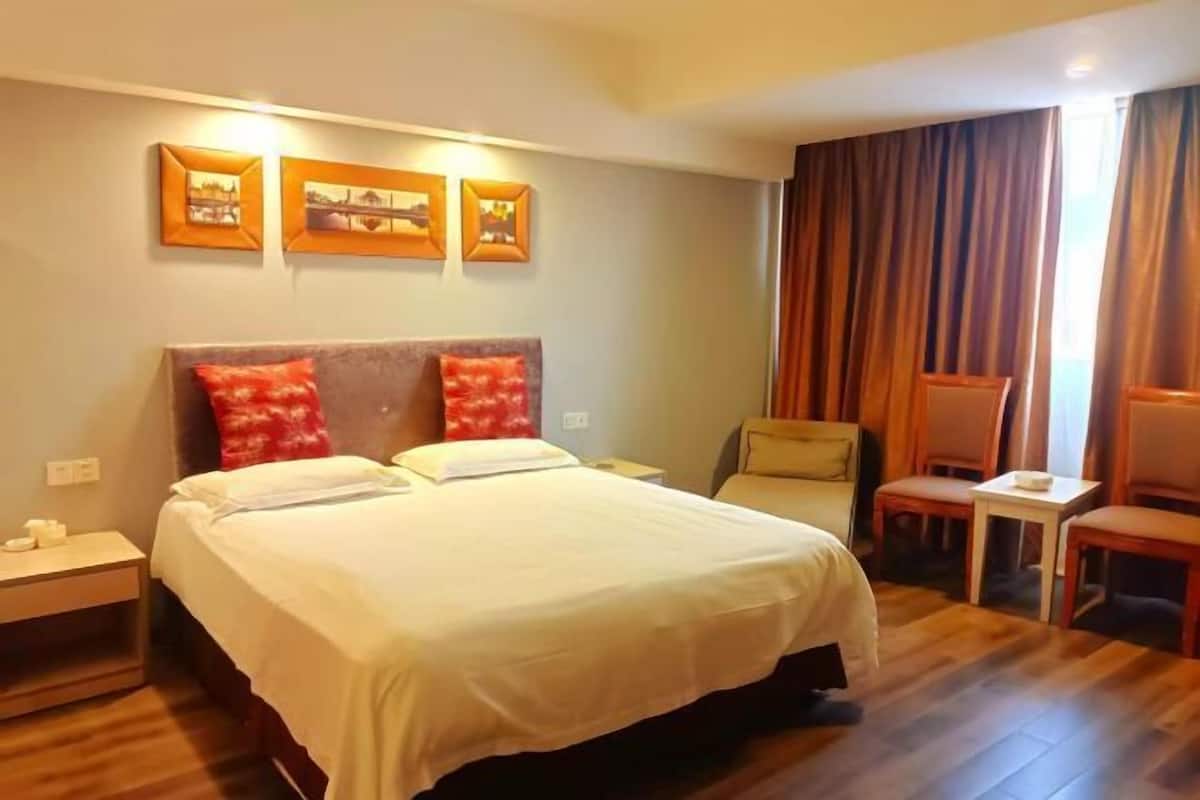 A hotel room with a large bed, a desk, a chair, and a window with curtains.
