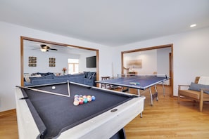 Un tavolo da biliardo con le bocce, un tavolo da ping pong e un divano in una stanza con pavimento in legno e pareti bianche.