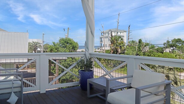 A covered outdoor balcony with white railings, a potted plant, and a white cushioned chair. - It's A Wonderful Life (Port St. Joe)